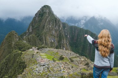 Sarışın kız mesafe içine bir gri kazak ve kot Machu Picchu, Peru, Ocak 2018 eliyle işaret ediyor. Dağlarda antik kenti