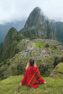 Kırmızı panço bir kız oturuyor ve Ocak, 2018 Peru Machu Pakchu bakar