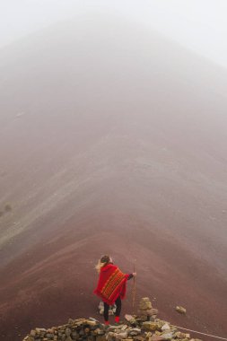Sisli havalarda kuru bir el ile bir kırmızı dağ arka plan sırtında ile sarışın kız duruyor