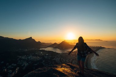 Brezilya, Rio de Janeiro. Şafak hill iki kardeş üzerinde toplantı. Büyük şehir, göl, okyanus, tepeler, dağlar manzarası. Turuncu-mavi renk siluet bakıyor şehir ve güneş bir kız.
