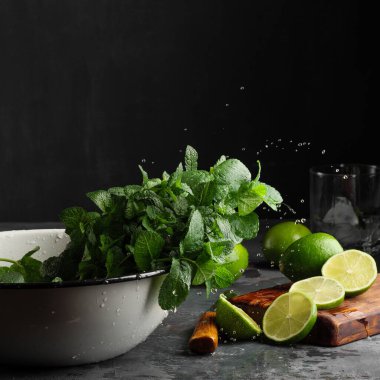Kırsal bir beyaz fincanda koyu arkaplana karşı sağda naneli bir kireç bulunur. Mojito malzemeleri..