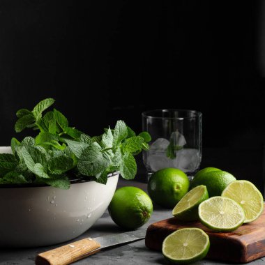 Kırsal bir beyaz fincanda koyu arkaplana karşı sağda naneli bir kireç bulunur. Mojito malzemeleri..