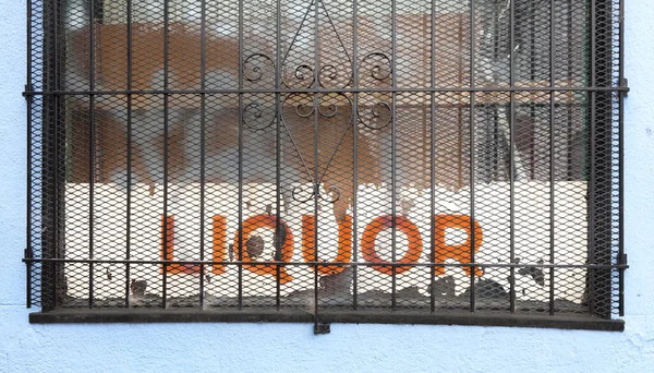 Shabby LIQUOR store sign behind rusty window security grate.