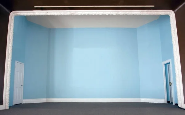 Empty auditorium stage with powder blue walls, side doors and carpeting.