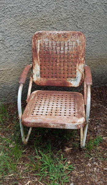 Vintage metal outdoor chair rusting against wall.