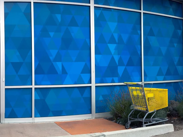 青い店の壁に対する黄色の食料品のカート — ストック写真