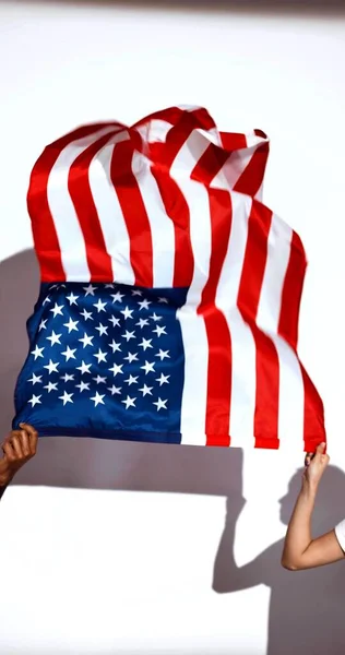 vertical photo of hands of a man and a woman which are holding a US flag