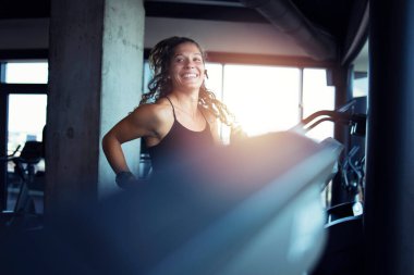 Spor salonunda koşu bandında egzersiz yapan gülümseyen bir kadın. Sağlıklı yaşam tarzı ve pozitif insanlar.