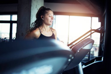 Spor salonunda koşu bandında egzersiz yapan gülümseyen bir kadın. Sağlıklı yaşam tarzı ve pozitif insanlar.