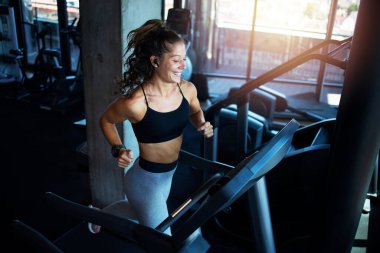 Spor salonunda koşu bandında egzersiz yapan gülümseyen bir kadın. Sağlıklı yaşam tarzı ve pozitif insanlar.