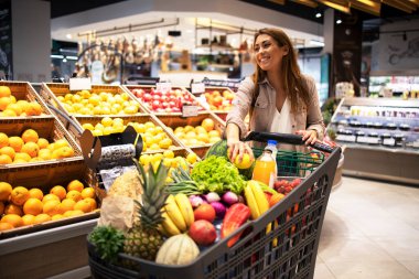 Alışveriş arabalarını iten ve süpermarkette raflardan meyve toplayan güzel bir kadın. Marketten yiyecek almak..