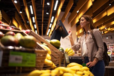 Süpermarketteki kadın meyvelerin ağırlığını ölçmek için self servis dijital ölçeği kullanıyor. Marketten yiyecek almak..