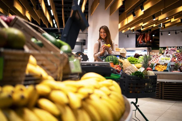 Brunette woman at grocery store with shopping cart buying fruit. Supermarket fruit department and female taking healthy food.