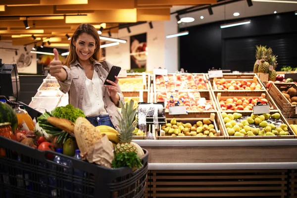 Mulher Com Telefone Inteligente Supermercado Nas Prateleiras Cheias Frutas Mercearia — Fotografia de Stock