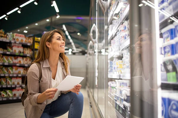 Beautiful woman with shopping list buying food in supermarket.