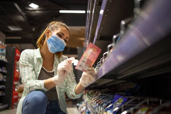 Grocery shopping during COVID-19 pandemic. Female person with mask and gloves buying food in supermarket.