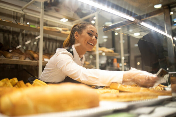 Woman preparing bread for sale in supermarket bakery department.