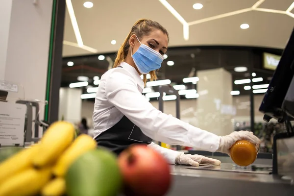 Corona virüsü salgınından dolayı riskli bir işte çalışırken süpermarkette çalışan kadın kasiyer hijyenik koruma maskesi ve eldiven takıyor..