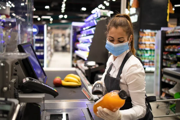 Süpermarketteki kasiyer maske takıyor ve Corona virüsüne karşı tamamen korunuyor. Covid-19 salgını sırasında çalışmak.
