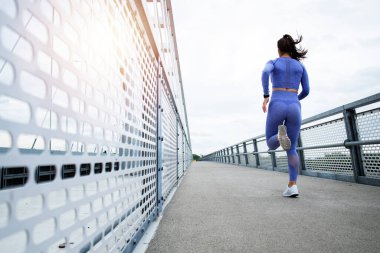 Güçlü vücut ve bacaklara sahip kadın koşucu köprüden ve eğitimden geçiyor. Spor ve eğlence..