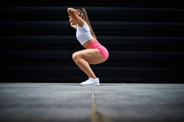 Uzun saçlı ve güçlü bacaklı kaslı seksi sporcu kadının spor salonunda siyah arka planda çömelmesi. Fitness ve vücut geliştirme.