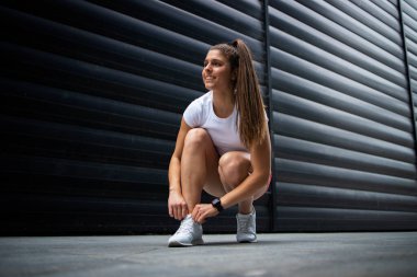 Uzun saçlı, güçlü bacaklı, spor salonundaki bağcıklarını siyah arka plana bağlayan kaslı seksi sporcu. Fitness ve vücut geliştirme.