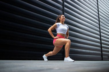 Uzun saçlı, güçlü bacaklı, spor salonunda esneyen ve ısınan kaslı seksi sporcu kadın sporcu. Fitness ve vücut geliştirme.