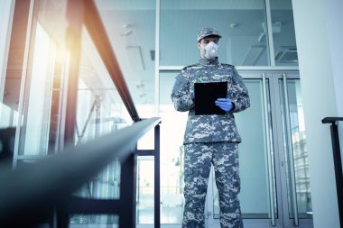 Askeri kamuflaj üniformalı asker lastik eldiven ve maskeyle hastanenin kapısının önünde nöbet tutuyor ve kimin girip çıktığını kontrol ediyor. Coronavirüs veya COVID-19 'a karşı savaşta askeri yardım.