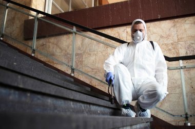 Beyaz kimya koruma giysisi giymiş bir erkeğin kamu koridorlarını dezenfekte etmesi ve son derece bulaşıcı korona virüsünü yaymayı durdurmak için adımlar atması. Coronavirüs veya COVID-19 'u durdurun..