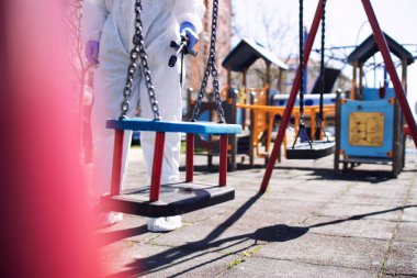 Çocuk parkı dezenfeksiyonu. Kamu sağlık hizmetleri. Beyaz elbiseli bir adam çocukları dezenfekte ederek yüksek derecede bulaşıcı koronavirüs ya da COVID-19 yayılmasını önlüyor..