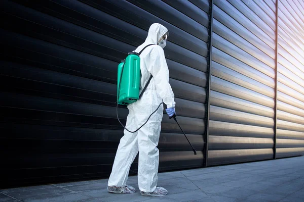 Shot of exterminator person in white chemical protection suit doing disinfection and pest control with sprayer to kill insects and rodents.