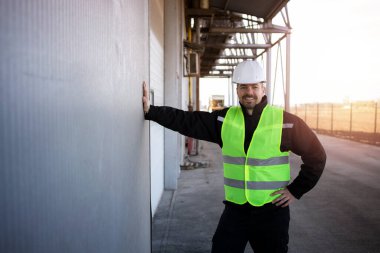 Endüstriyel binanın önünde duran koruyucu elbiseli fabrika işçisinin portresi. Fabrikanın dış tarafı..