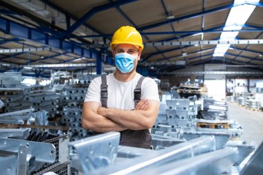 Üniformalı fabrika işçisi portresi ve endüstriyel üretim fabrikasında yüz maskesi takan bir kasket. COVID-19 salgını sırasında çalışanlar.