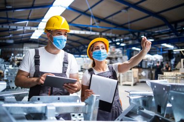 Yüz maskeli fabrika işçileri Corona virüsüne karşı korunuyorlar. Fabrikada üretimin kalitesini kontrol ediyorlar. COVID-19 salgını sırasında çalışanlar.