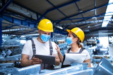 Yüzü maskeli endüstriyel işçiler Corona virüsüne karşı korunuyor. Fabrikada üretimin sonuçlarını analiz ediyorlar. COVID-19 salgını sırasında çalışanlar.