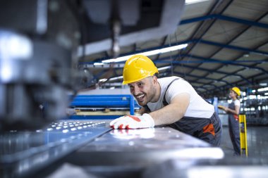 Üniformalı fabrika işçisi ve üretim bandında çalışan sanayi makinası. Endüstride çalışan insanlar.
