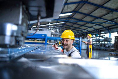 Üniformalı fabrika işçisi ve üretim bandında çalışan sanayi makinası. Endüstride çalışan insanlar.