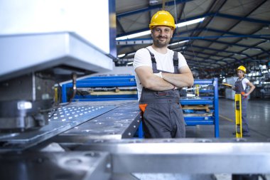 Üniformalı fabrika işçisinin portresi üretim hattında endüstriyel makinenin yanında duruyor. Endüstride çalışan insanlar.