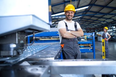 Üniformalı fabrika işçisinin portresi üretim hattında endüstriyel makinenin yanında duruyor. Endüstride çalışan insanlar.
