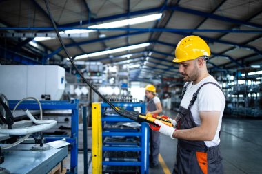 Üniforma giyen fabrika işçisi ve üretim salonunda düğmeye basan endüstriyel makine. Çalışan endüstriyel üretim makinesi üzerinde çalışıyor..