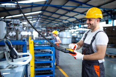 Üniforma giyen fabrika işçisi ve üretim salonunda düğmeye basan endüstriyel makine. Çalışan endüstriyel üretim makinesi üzerinde çalışıyor..