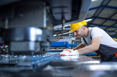 Koruyucu ekipmanı olan ve fabrika üretim hattında endüstriyel makine üzerinde çalışan erkek işçi..