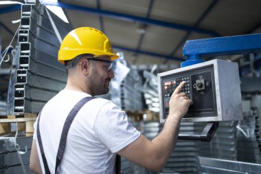 Fabrika işçisi endüstriyel makineyi çalıştırıyor ve parametreleri bilgisayarda ayarlıyor.