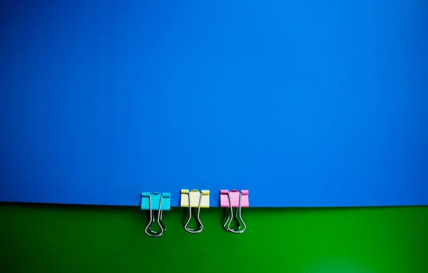 Multicolored blue green background with three office clamps