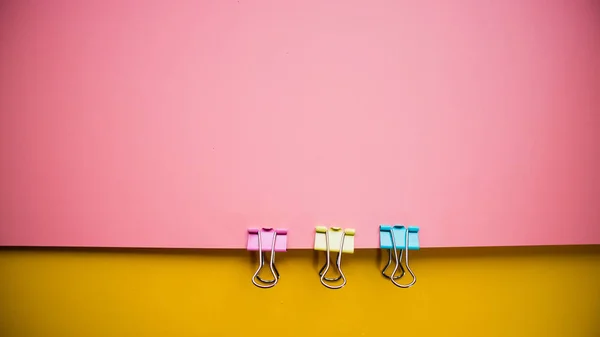 Multicolored pink yellow background with three office clamps