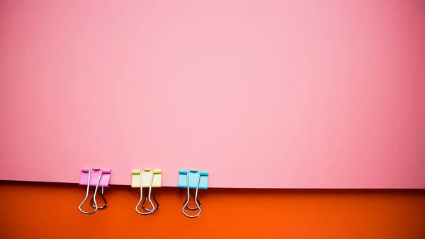 Multicolored pink red background with three office clamps