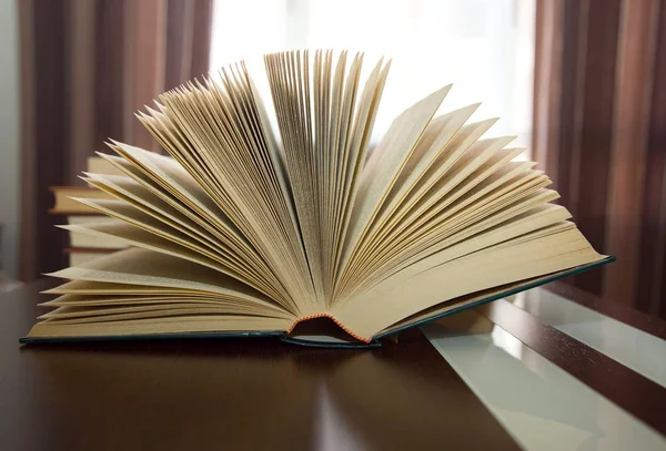 Dik open boek in ventilator op houten tafel tegen achtergrondverlichting — Stockfoto