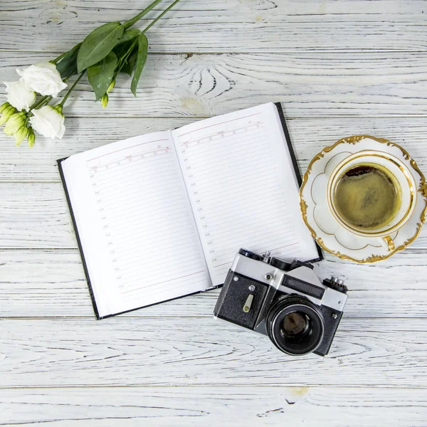 white ustom, diary, antique camera and cup of coffee and saucer on a light background, flat lay