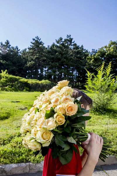 young man with a bouquet of tender roses on his shoulder goes on a sunny day