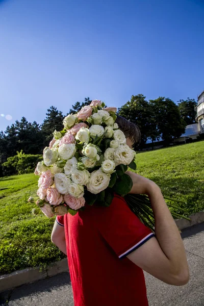 young man with a bouquet of tender roses on his shoulder goes on a sunny day